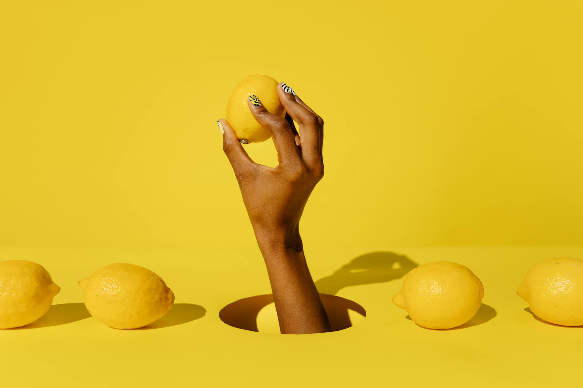 A hand holding a fresh lemon against a vivid yellow background, conveying freshness and renewal