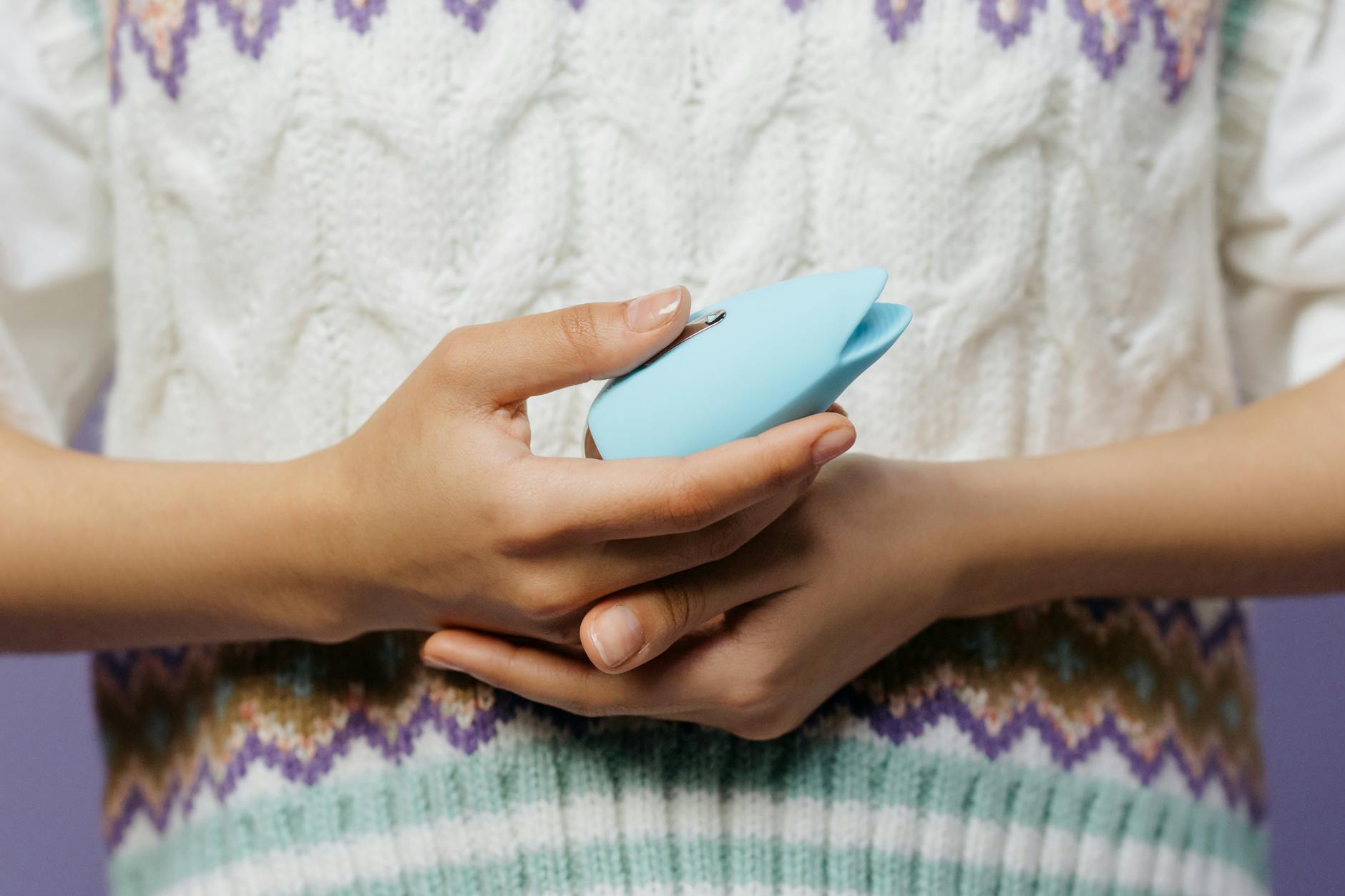 A hand holding a blue personal massager against a knitted sweater.